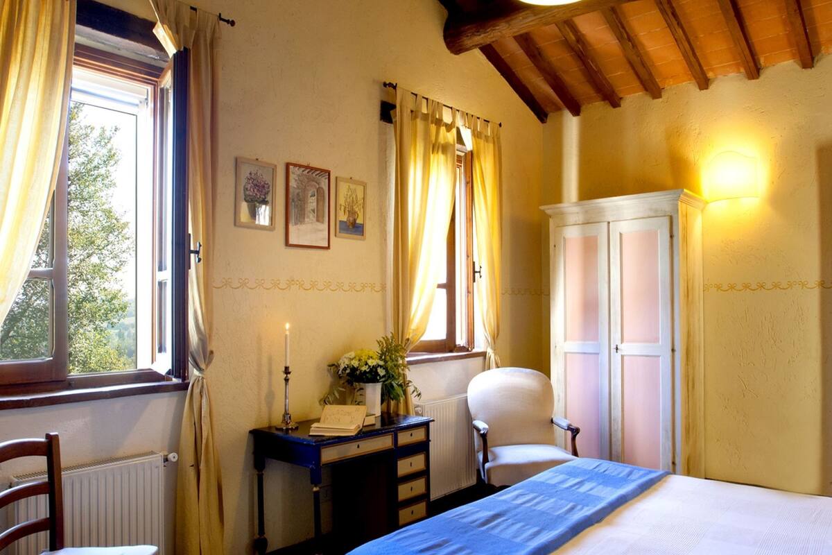 Une chambre à coucher comprenant un lit, un bureau, une chaise, une armoire et une fenêtre avec des rideaux.