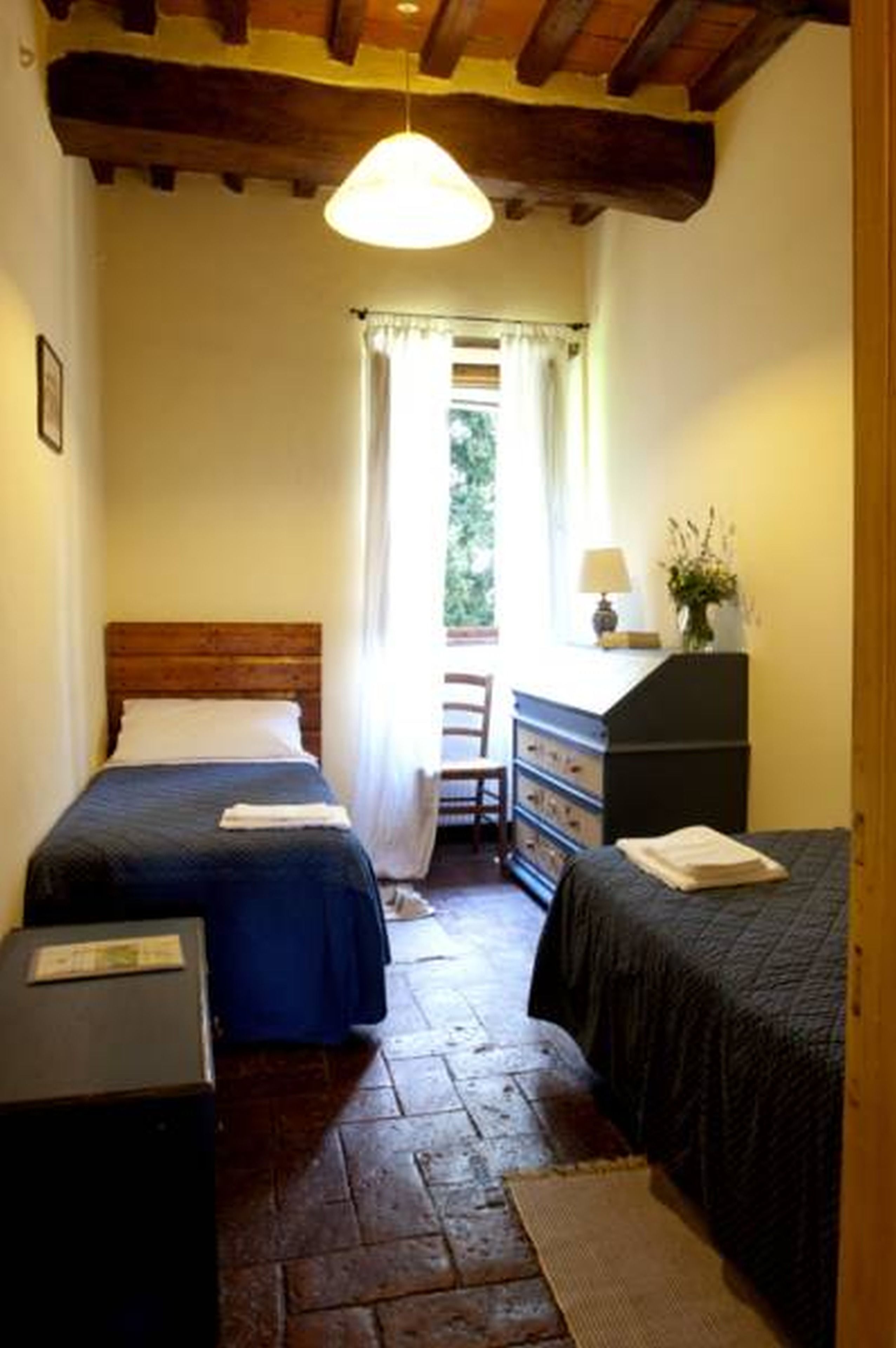A small, cozy room with two beds, a dresser, a desk, and a window with curtains.