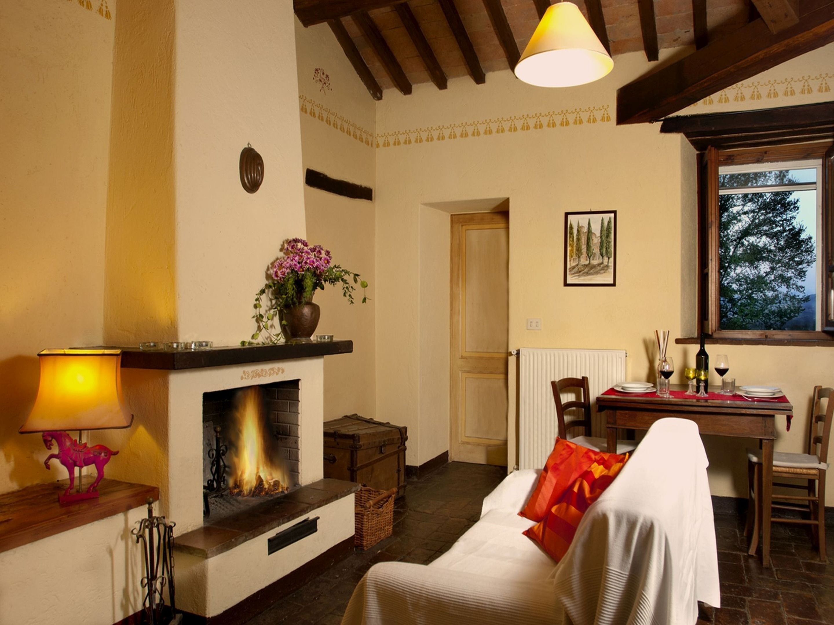A cozy room with a fireplace, a dining table with chairs, and a window with a view of trees.