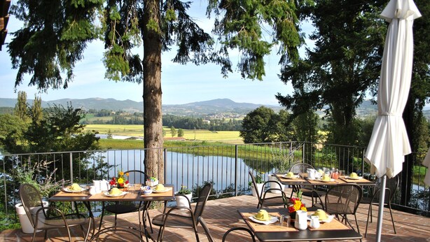 Un espace extérieur aménagé pour les repas, avec des tables et des chaises, offrant une vue sur un lac et des collines.