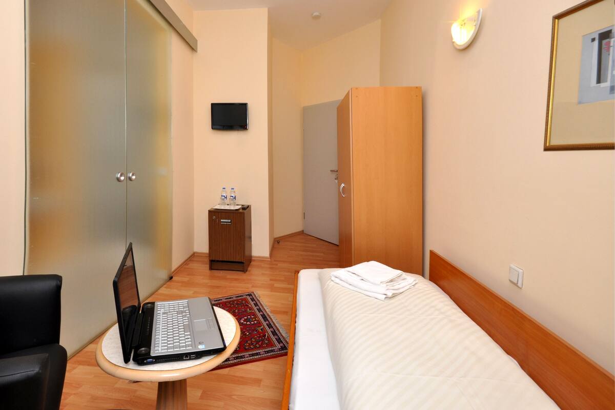 Une chambre d’hôtel comprenant un lit, un bureau avec un ordinateur portable, une armoire, une télévision et un petit meuble de rangement.