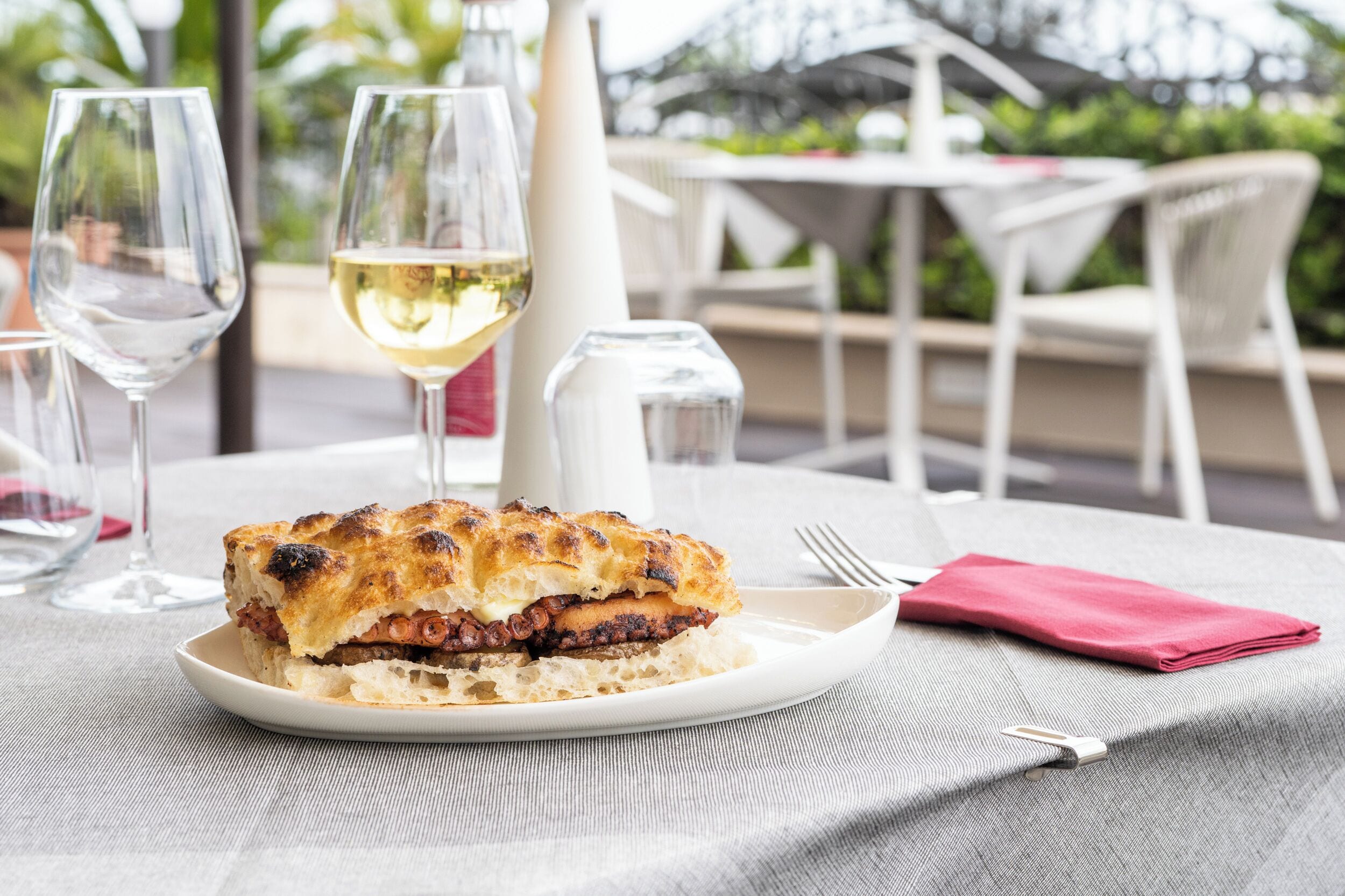 Una mesa con un plato de comida, una copa de vino blanco y un mantel doblado.