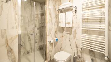 A bathroom with a glass-enclosed shower, a white toilet, a sink, and a towel rack with towels.