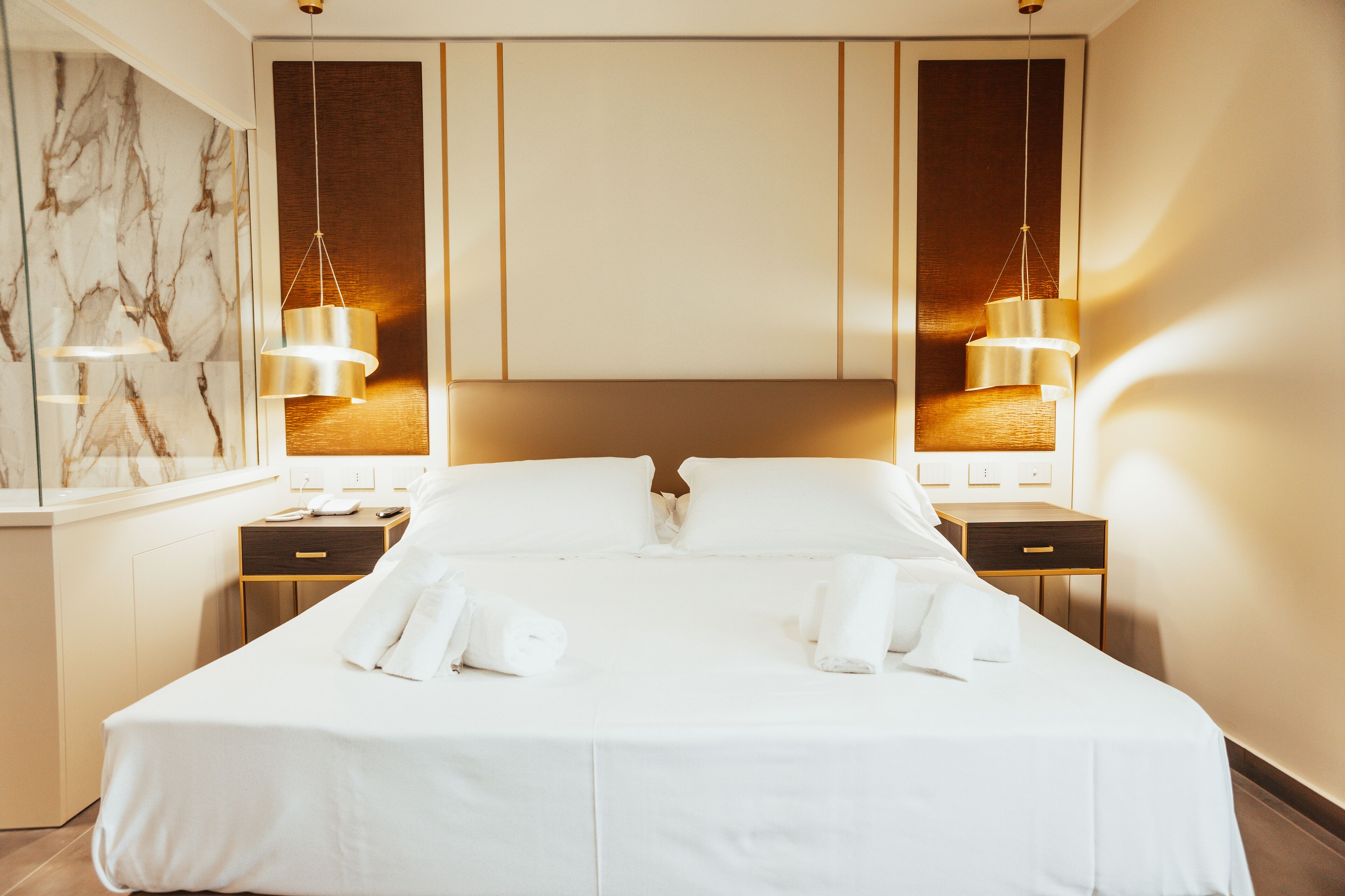 Een hotelkamer met een groot bed, twee nachtkastjes, een marmeren wand en twee wandlampen.