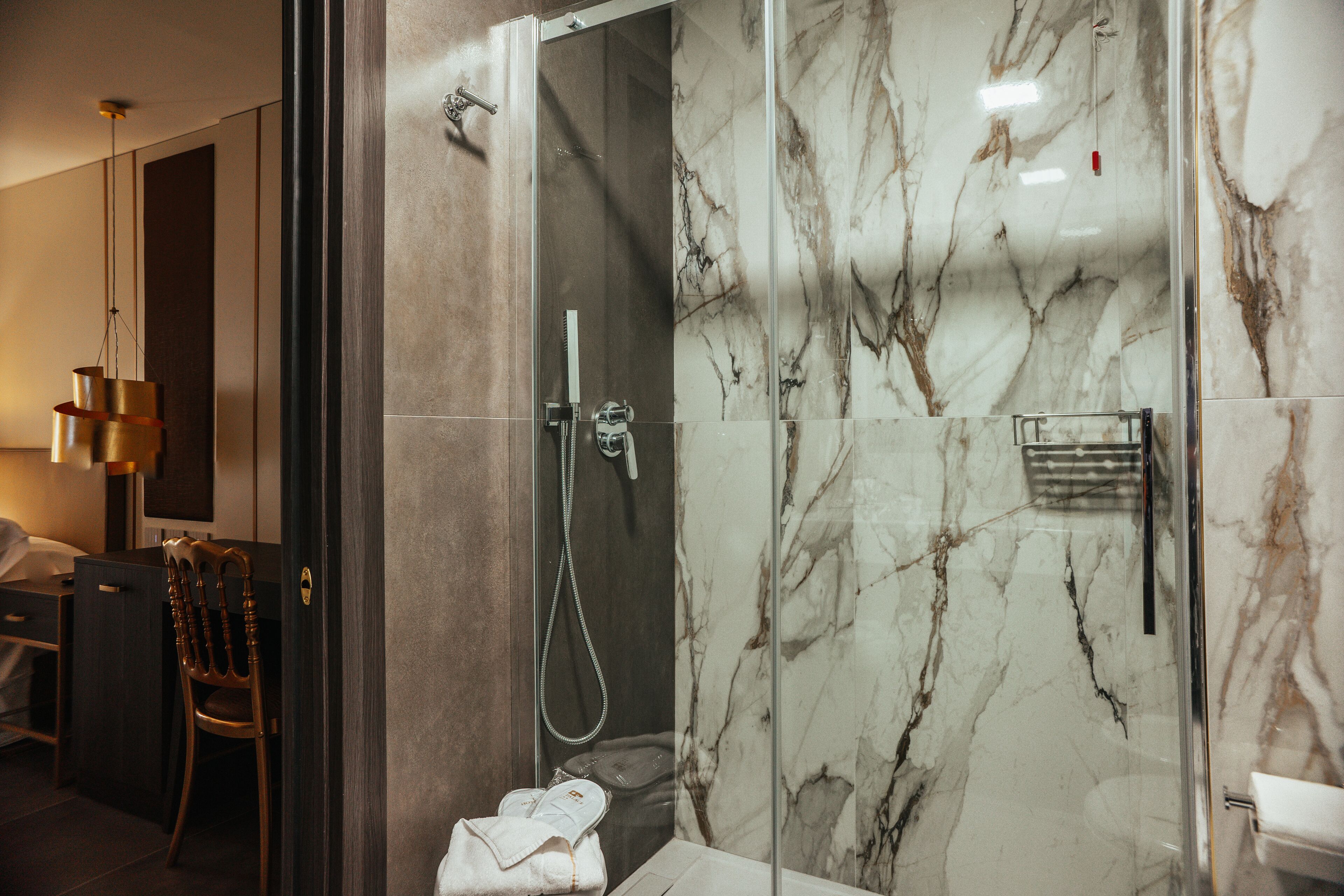 Un baño moderno con ducha de vidrio, paredes de mármol, una silla de madera y un perchero para toallas.