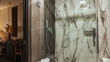 Un baño moderno con ducha de vidrio, paredes de mármol, una silla de madera y un perchero para toallas.