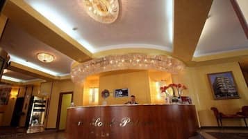 Un'area di reception di un hotel con una scrivania in legno, un lampadario e un quadro appeso al muro.