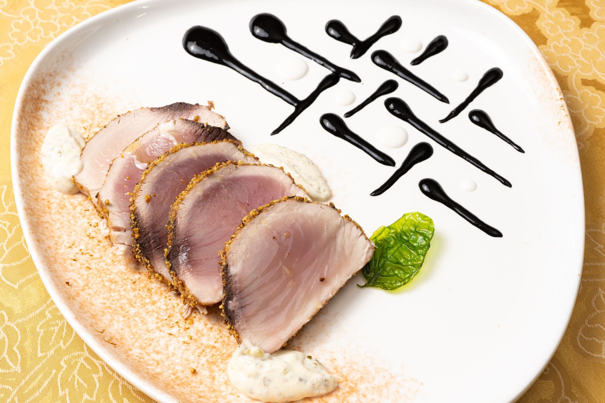 A plate of sliced meat with a garnish and sauce.
