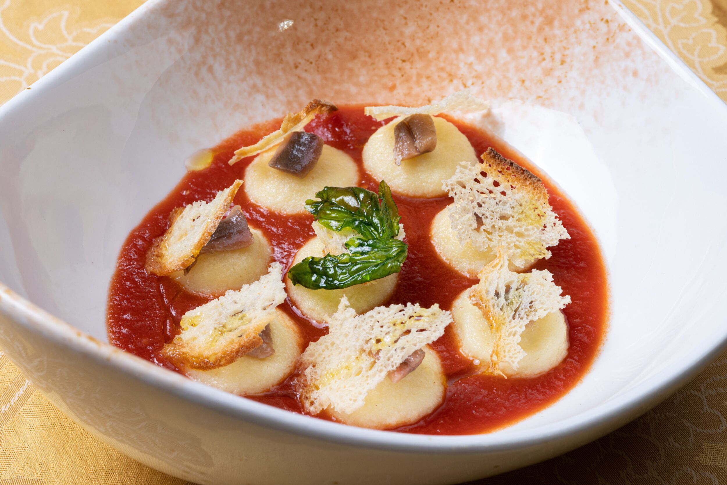 A bowl of soup with bread and a basil leaf.