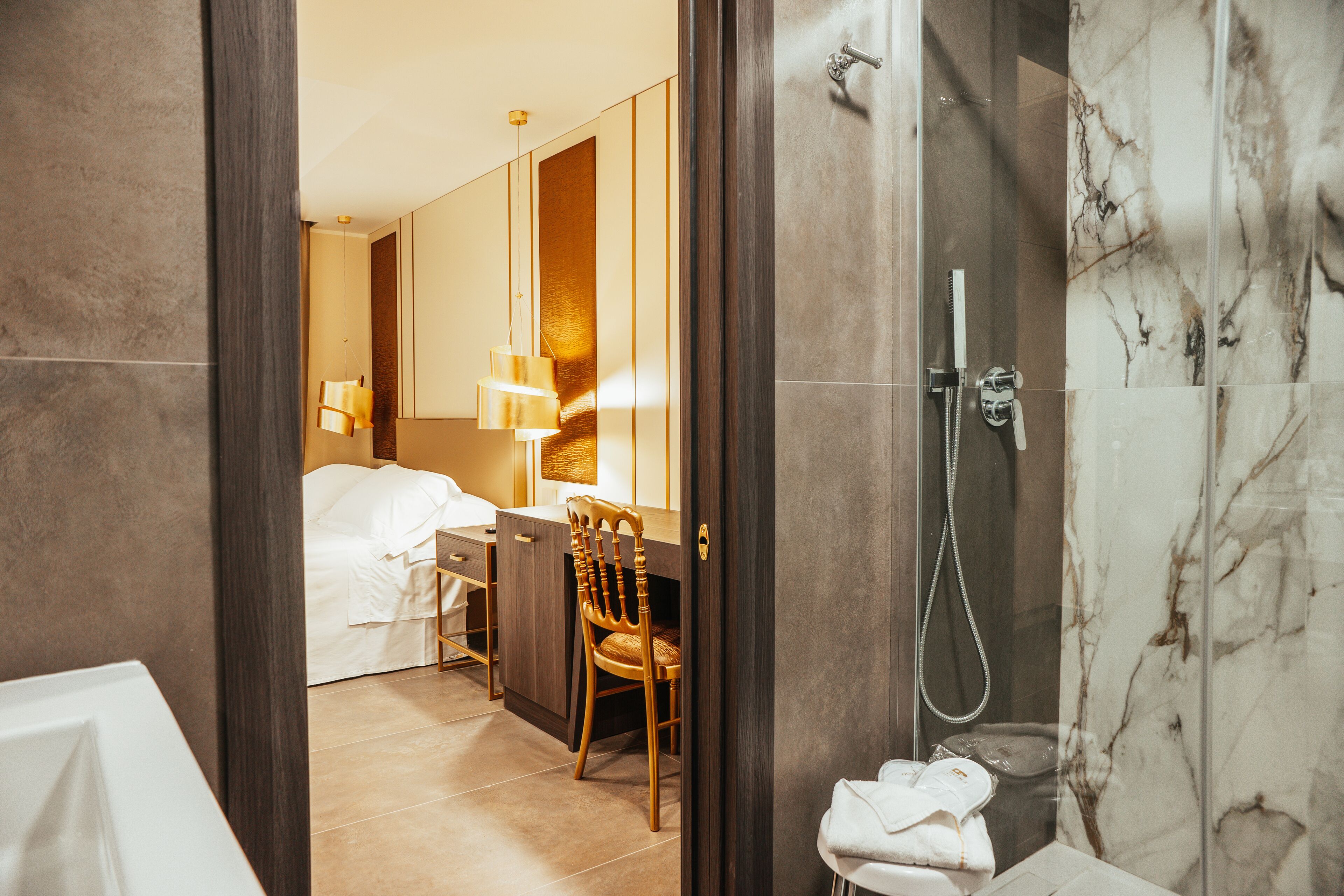 Un baño de hotel moderno con ducha, inodoro y lavabo. Hay una silla de madera y un escritorio con lámpara.