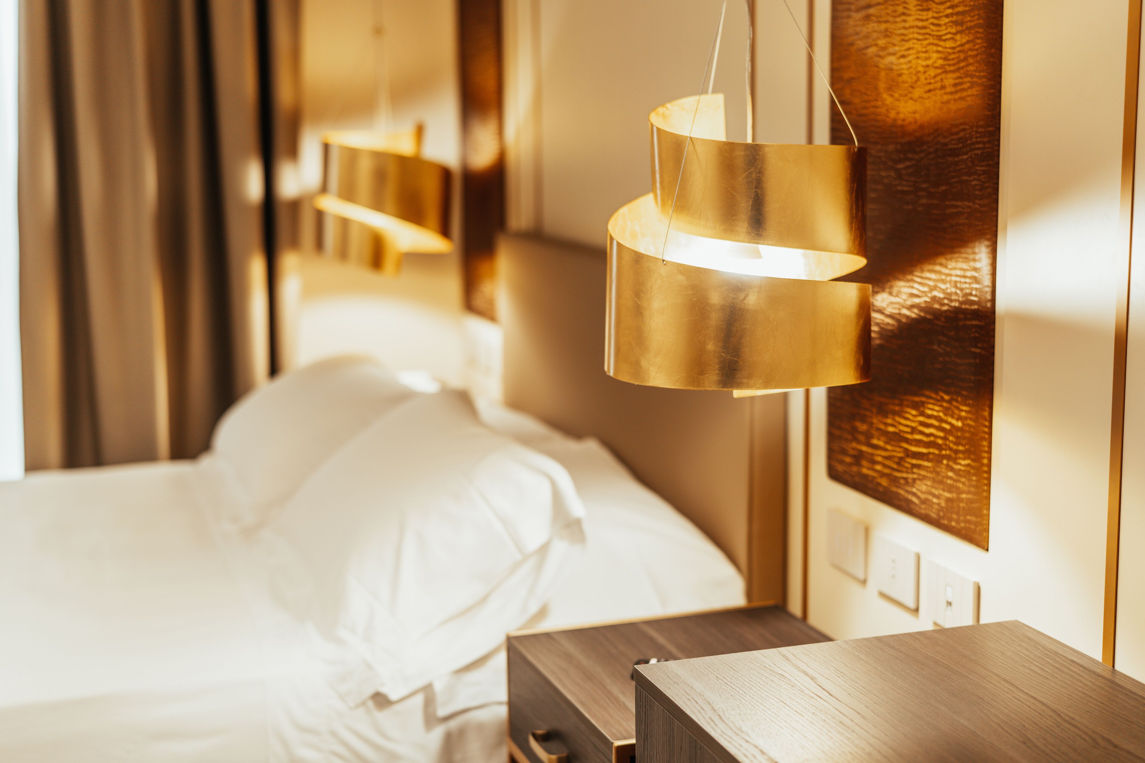 Una habitación de hotel con una cama bien hecha, una mesita de noche de madera y una lámpara de pared.