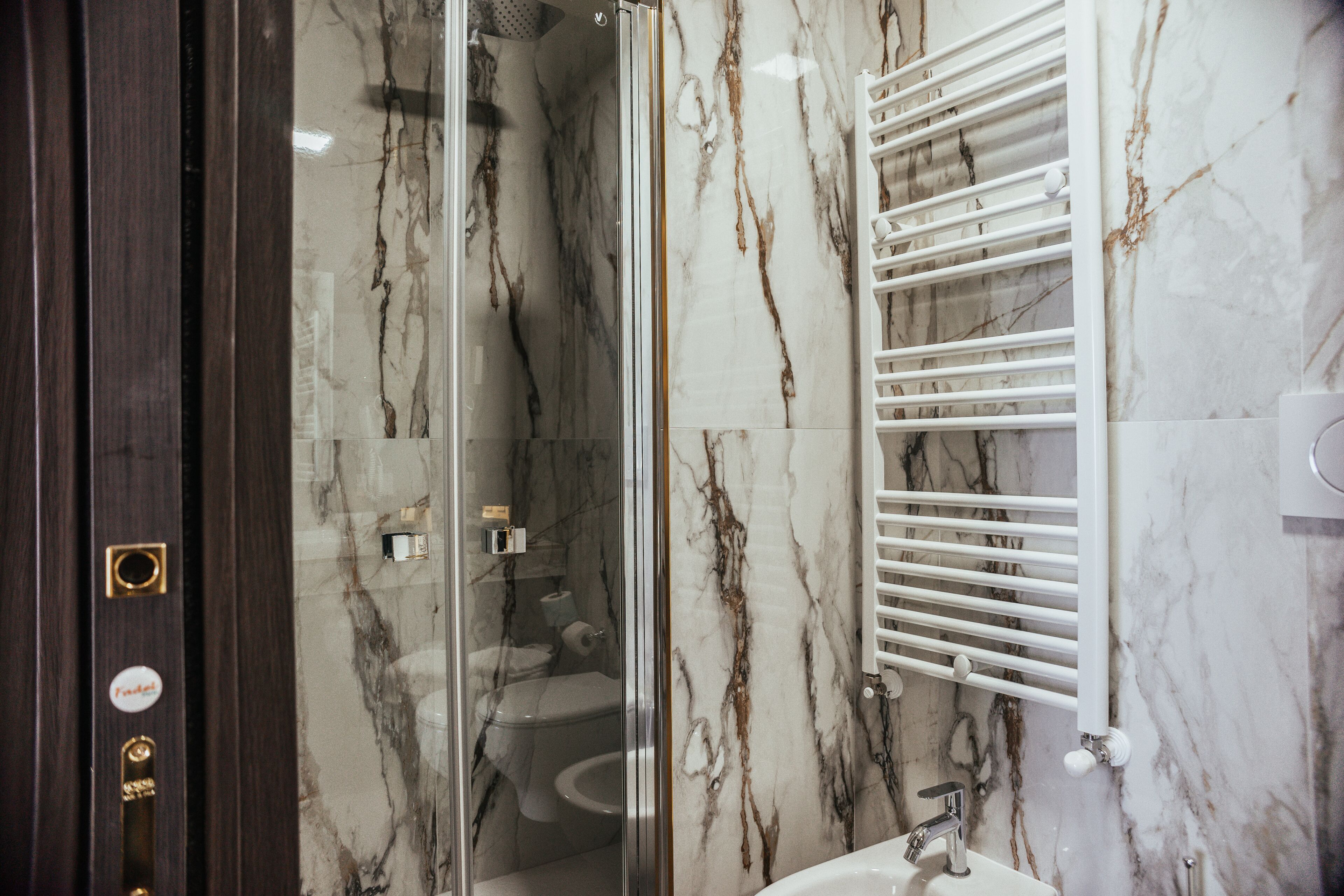 A bathroom with a glass-enclosed shower, a white sink, and a marble wall.