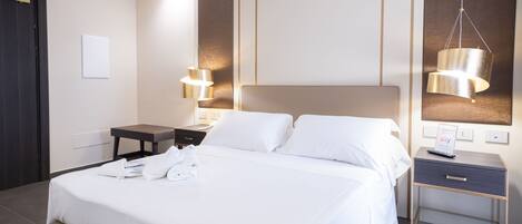 A modern hotel room with a large bed, bedside tables, a desk, and a hanging light fixture.