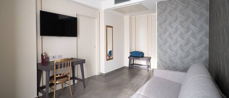 A modern hotel room with a flat-screen TV, a desk with a chair, a sofa, and patterned wallpaper.