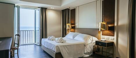A modern hotel room with a large bed, bedside table, desk, and chair.