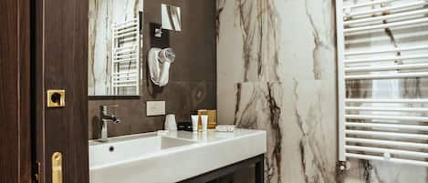 A bathroom with a marble wall, a white sink, a mirror, and a towel rack.