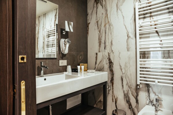 A bathroom with a marble wall, a white sink, a mirror, and a towel rack. - Hotel Palace (Catanzaro)