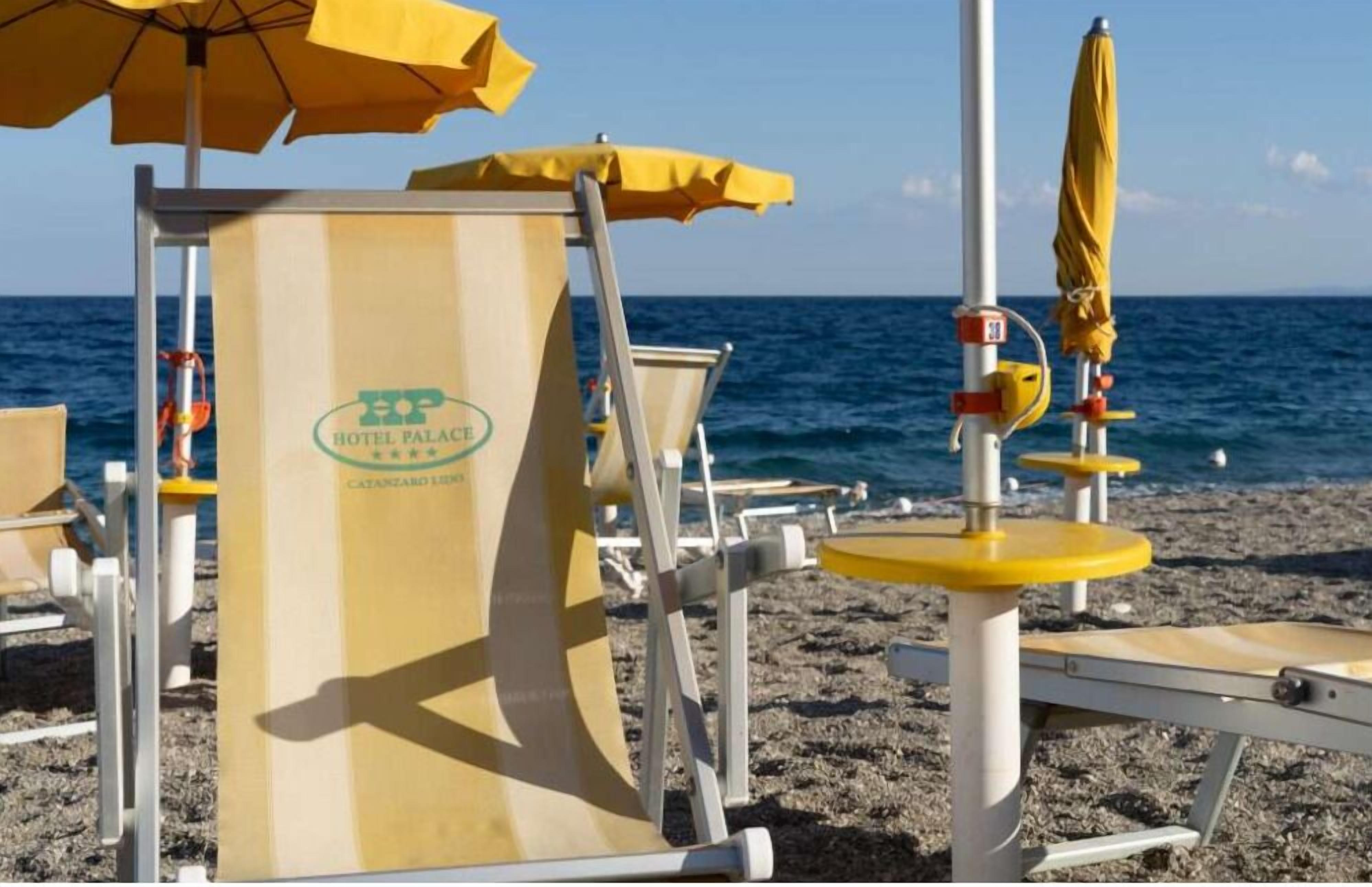 A beach chair with a yellow umbrella, a lifebuoy, and a sign for Hotel Palace Catanzaro Lido.