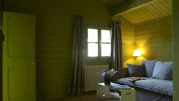 A room with a green door, a window with curtains, a sofa, a table with a lamp, and a radiator.
