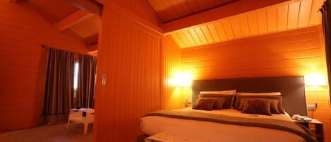 Un dormitorio acogedor con techo de madera, una cama grande con almohadas, una mesita de noche y una silla.