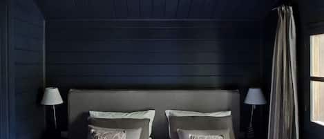A bedroom with a wooden headboard, two bedside tables with lamps, and a window with curtains.
