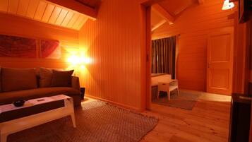 Ein gemütliches Zimmer mit Holzboden, einem weißen Sofa, einem kleinen Tisch und einer Lampe.