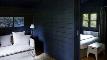 Una habitación con una cama, una mesita blanca, una lámpara y una ventana con cortinas.