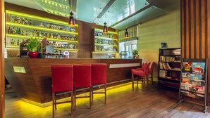 A bar area with wooden bar counter, red bar stools, and shelves stocked with bottles. - Hotel Royal (Kraków)
