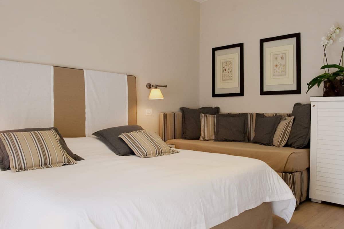 A hotel room with a large bed, a sofa, and two wall-mounted lamps.