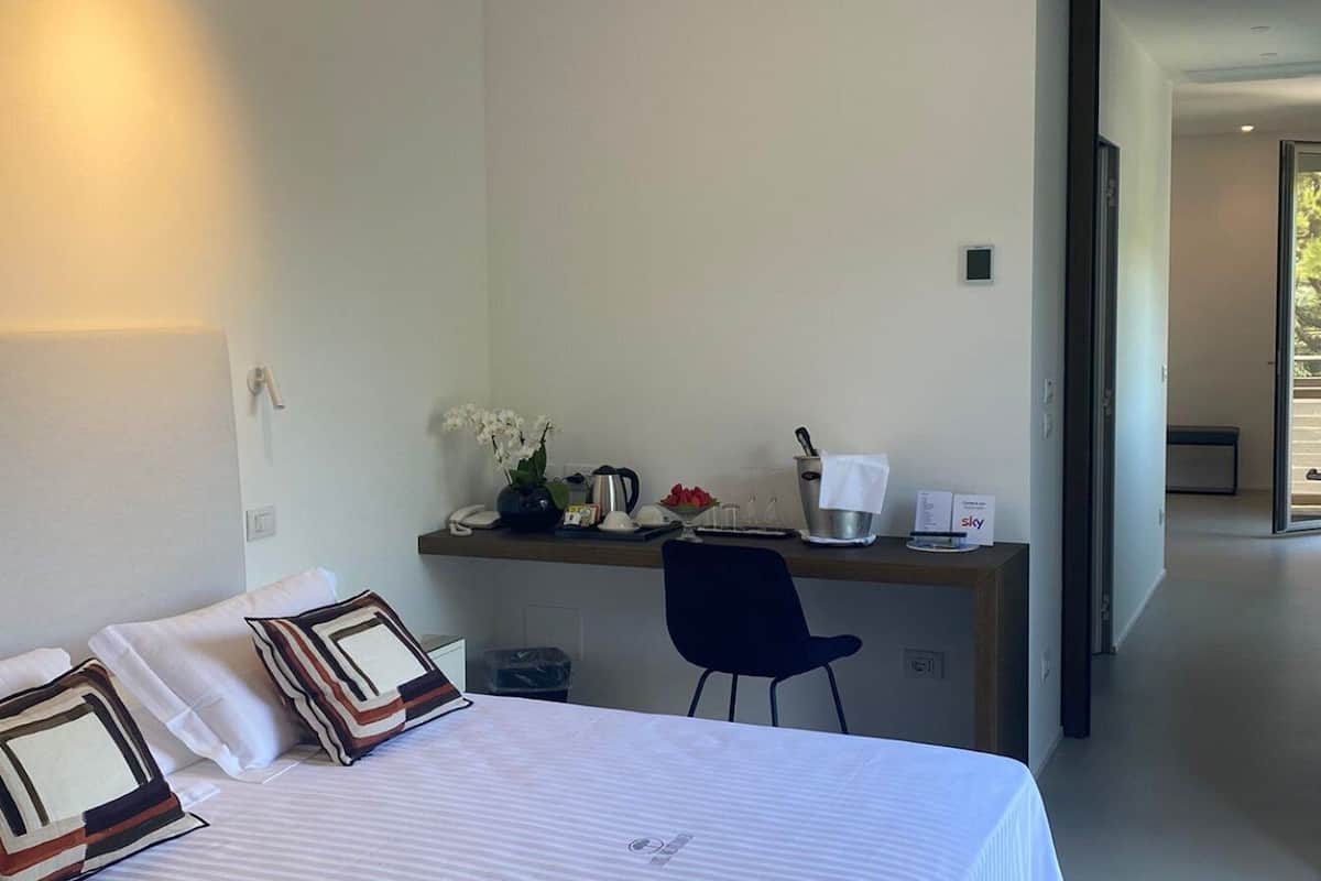 A hotel room with a bed, a desk with a chair, a coffee maker, and a vase with flowers.
