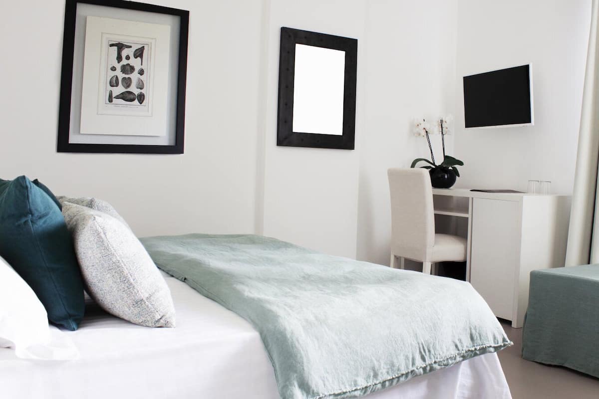 A hotel room with a bed, a desk, a chair, and a TV on the wall.