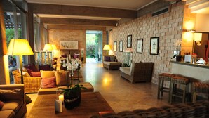 A spacious living area with a brick wall, wicker furniture, and a view through a glass door. - Hotel Mediterraneo (Jesolo)
