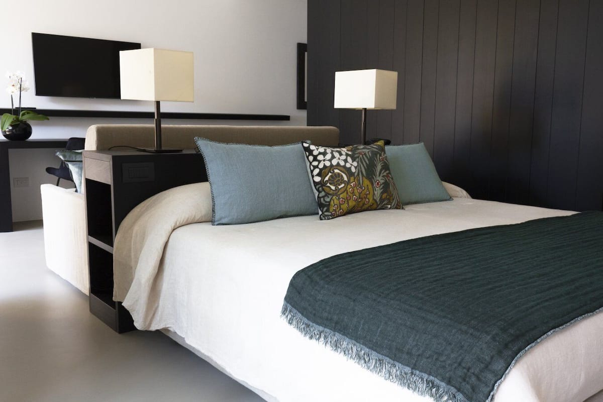 A modern hotel room with a bed, two bedside lamps, a flat-screen TV, and a small side table with a vase of flowers.