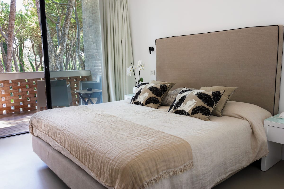 A bedroom with a large bed, two pillows, a nightstand, and a view of trees through a window.