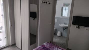 Ein Schlafzimmer mit Bett, ein Badezimmer mit Waschbecken und Toilette sowie ein an der Wand befestigter Fernseher.