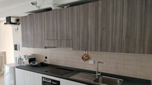 Una cocina moderna con gabinetes grises, encimera negra, lavavajillas integrado, pileta de acero inoxidable y salpicadero de azulejos blancos.