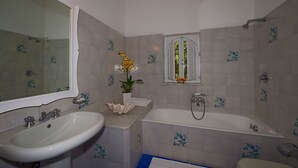 A bathroom with a sink, bathtub, and window with flowers. - Villa Rosa (Positano)