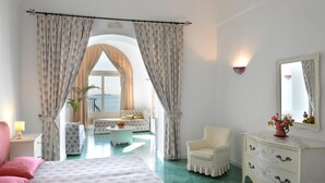 A bedroom with a bed, a chair, a dresser, and a view of the outdoors through a window. - Villa Rosa (Positano)