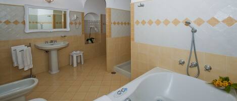 Un baño con bañera, lavamanos e inodoro. Hay toallas colgadas en la pared, un taburete pequeño y un florero.