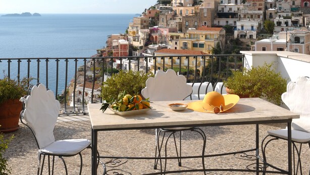 A terrace with a table set for two, overlooking a coastal town with colorful buildings. - Villa Rosa (Positano)