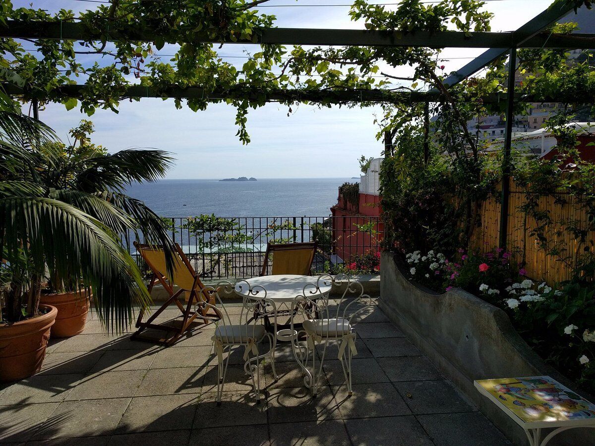A patio with a table and chairs, potted plants, and a view of the sea.