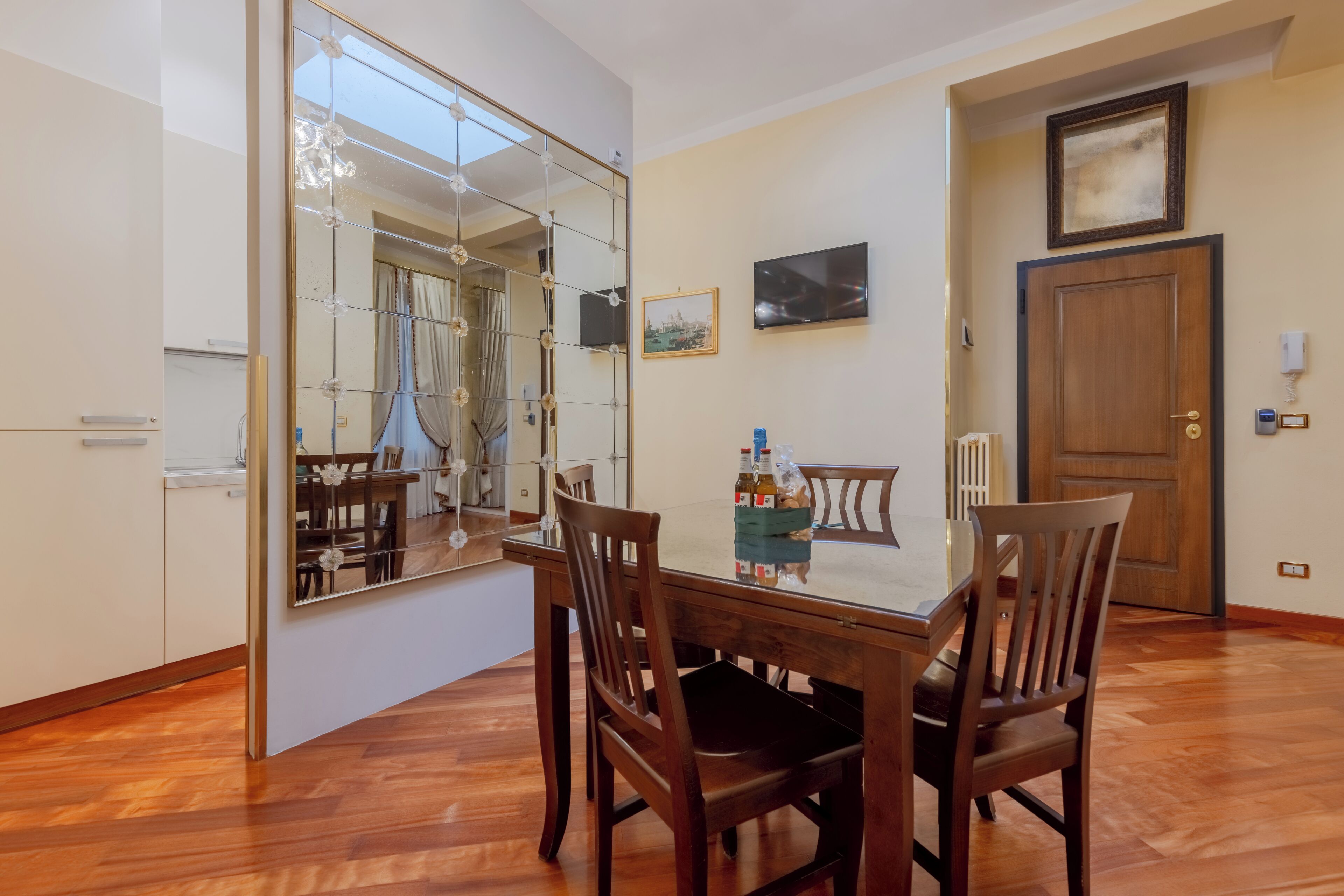 Un coin repas avec une table en bois, des chaises, un grand miroir et une porte en bois.