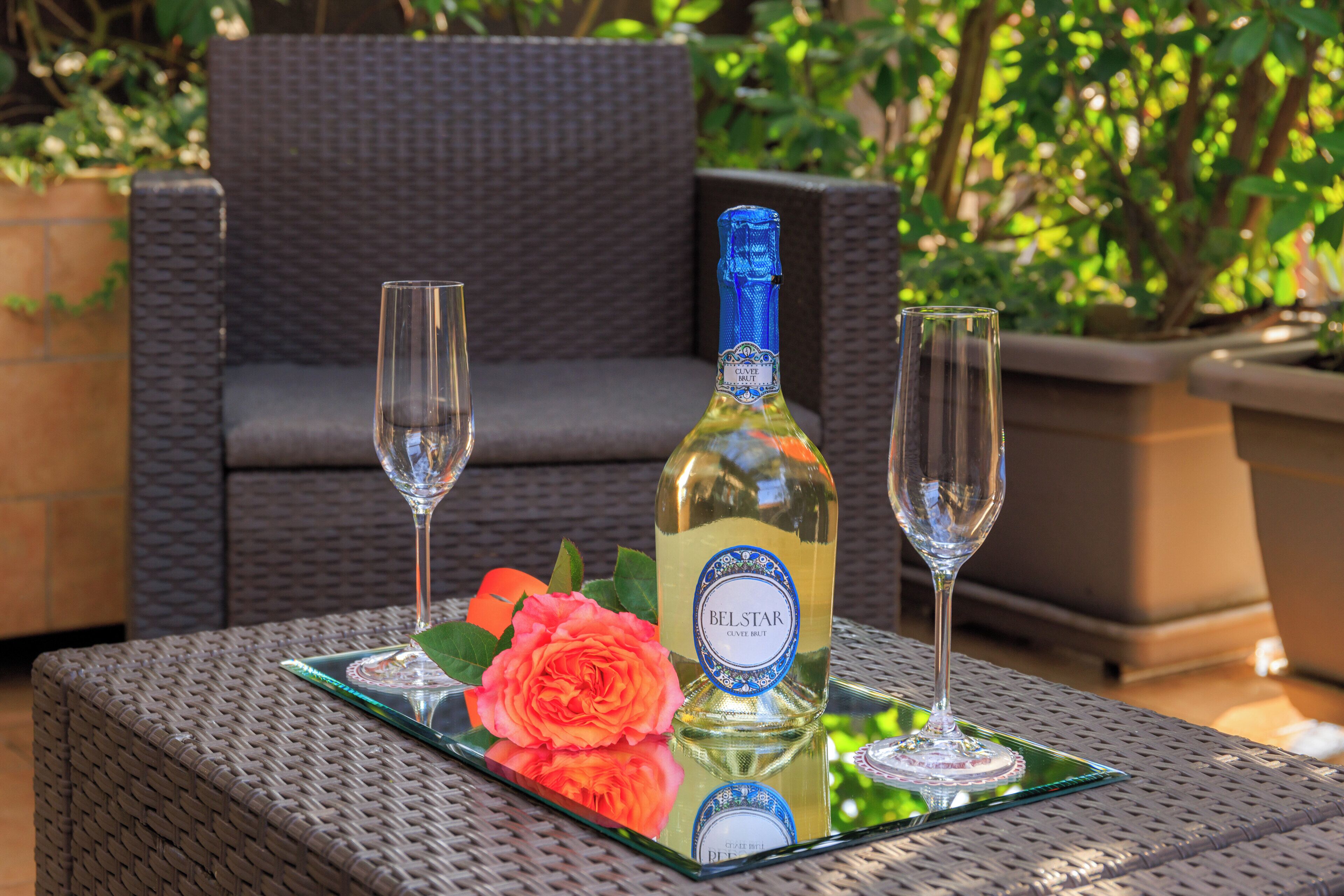 A bottle of Belstar wine on a glass tray with two glasses and a rose.
