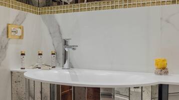 Un bagno con un lavandino bianco, uno specchio con cornice dorata e una rosa gialla in un vaso di vetro.