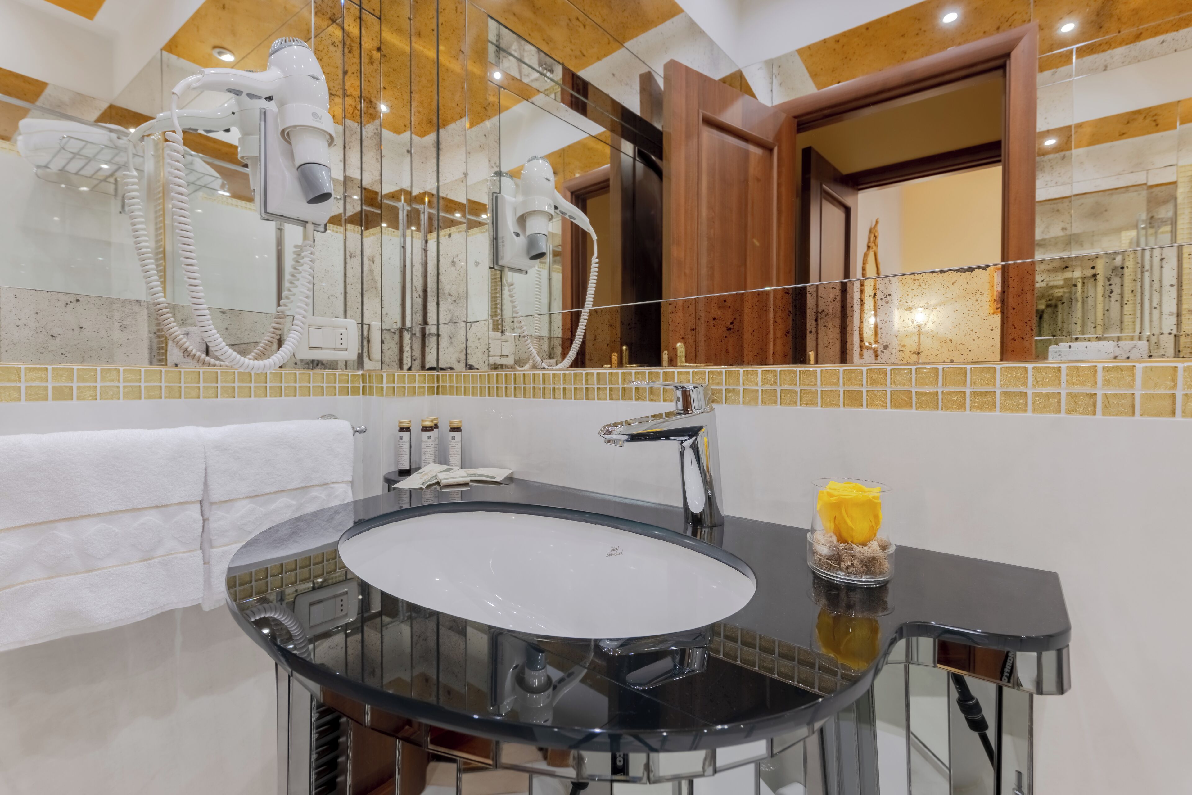A bathroom with a black sink, a mirror, and a hairdryer mounted on the wall.