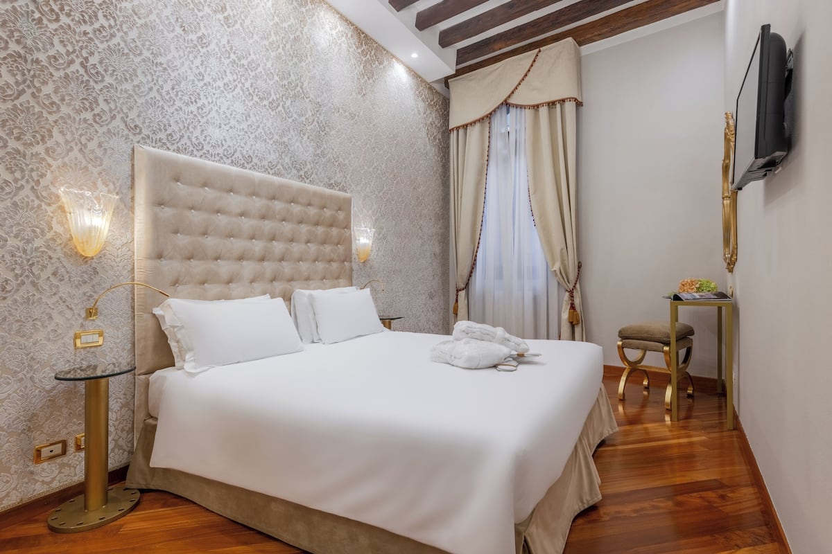 A neatly made bed with white linens, a tufted headboard, and a bedside table with a lamp.