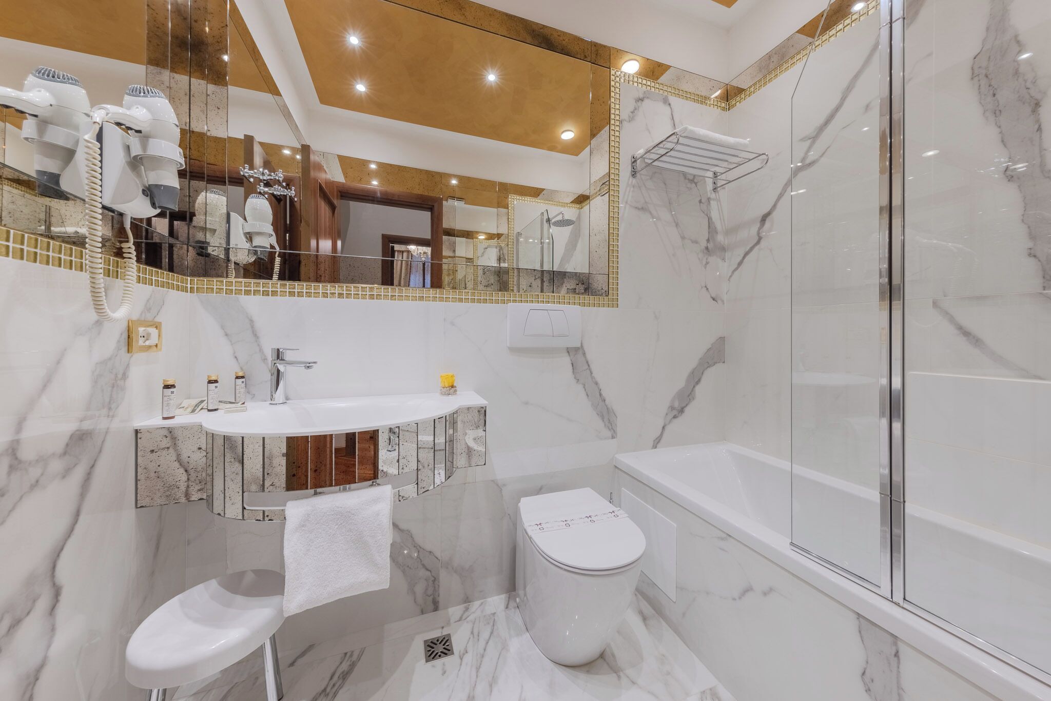 A modern bathroom with a marble vanity, a toilet, and a glass-enclosed shower.