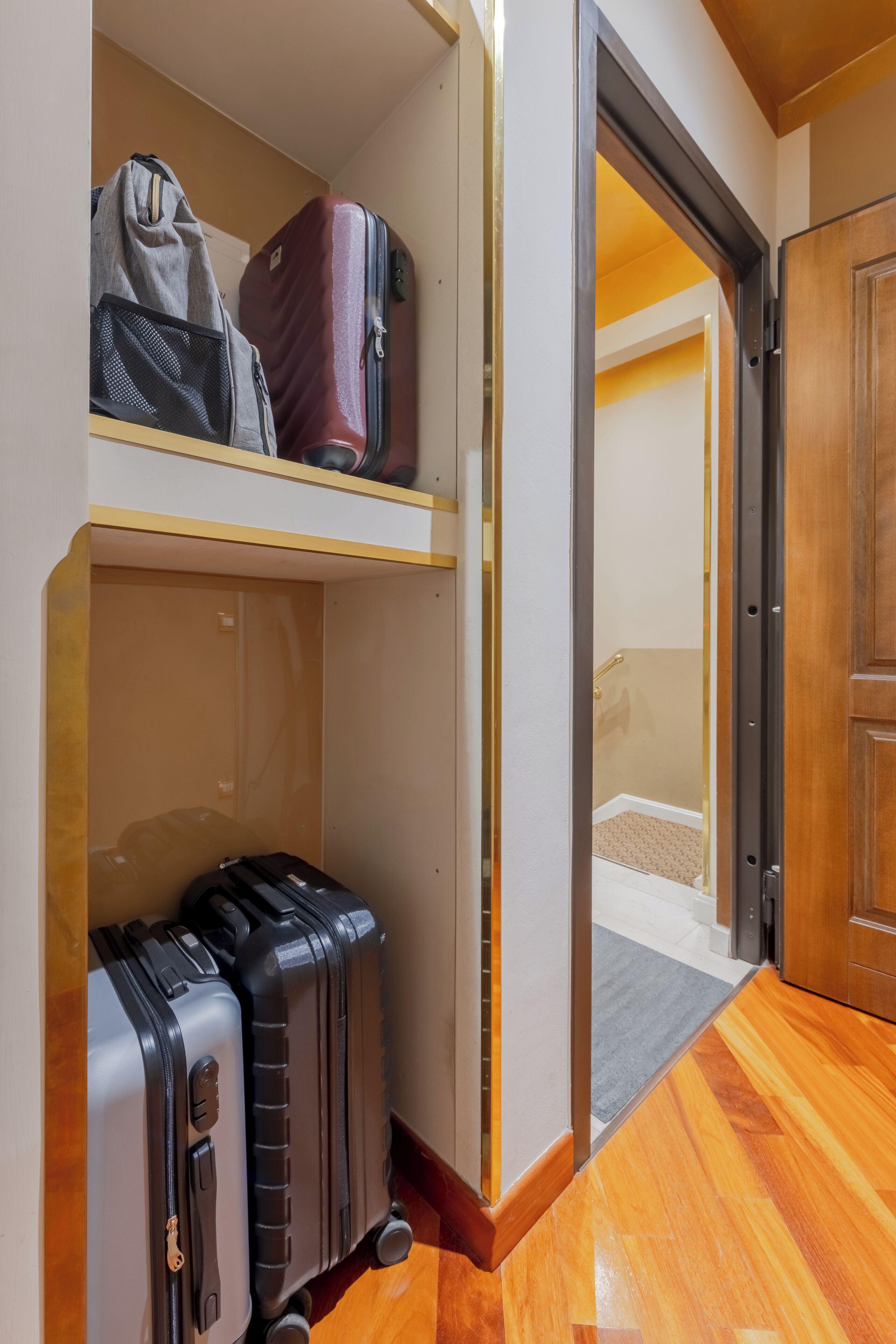 A hallway with wooden flooring, a door, and a shelf with luggage.