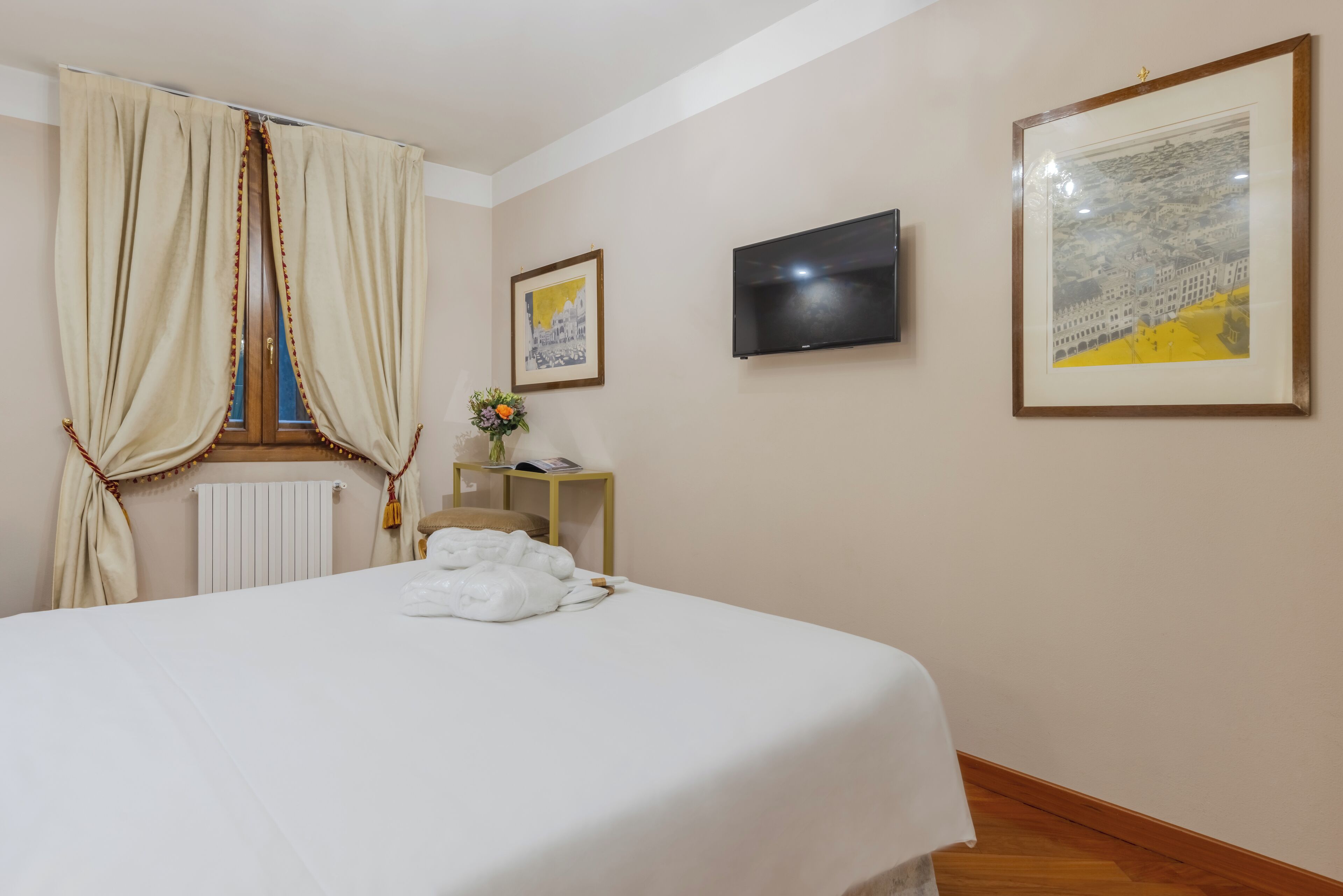 Een hotelkamer met een bed, een televisie en twee foto’s in lijsten aan de muur.