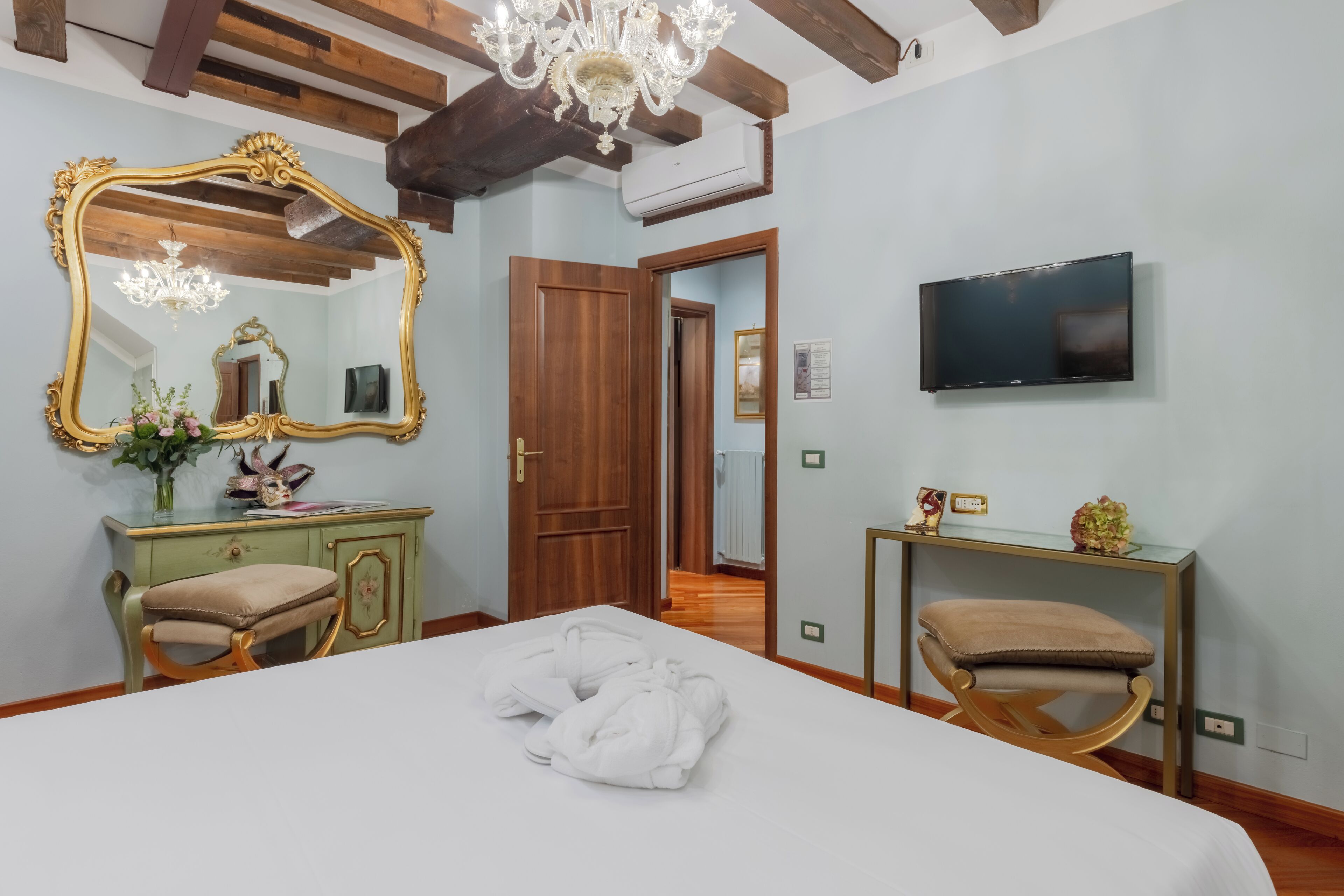 A hotel room with a large bed, a vanity with a mirror, a television, and a wooden ceiling.